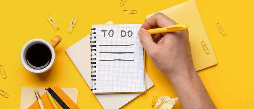 Male hand with to-do list, notebooks, cup of coffee and stationery on yellow background