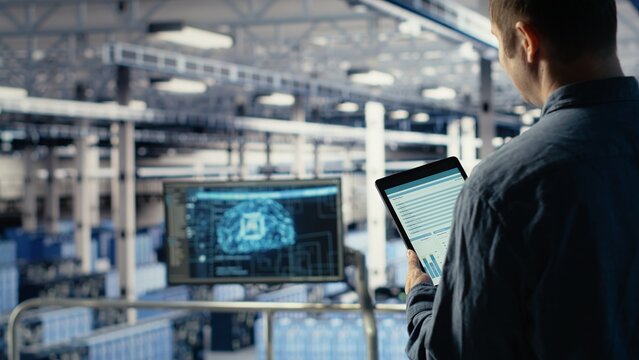 Server room IT expert swiping on tablet touchscreen to read data charts, monitoring equipment health. Admin reviews analysis metrics graphs on device to make sure data center meets goals, camera B