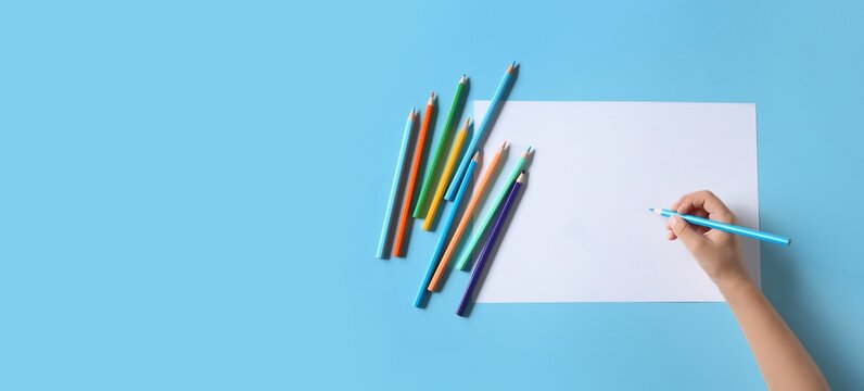 Hand with blank sheet of paper and colorful pencils on blue background with space for text