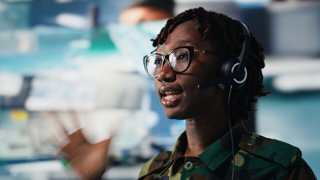 Close up of army telecommunications operator uses tablet and headset to manage secure military communications. Soldier coordinates mission support from command center with surveillance technology