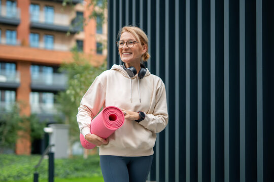 Mature woman smiling carrying yoga mat for fitness - Powered by Adobe