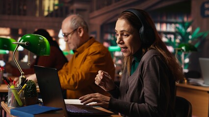 Woman listens to loud music on headset and disturbing other people in the library, senior man asking her to keep the volume low, breaking the library rules. Careless person singing.