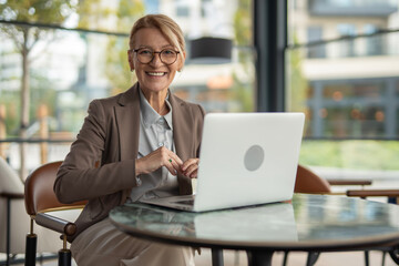 Smiling mature businesswoman working on laptop in modern cafe
