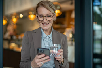 Smiling mature woman using smartphone with water glass