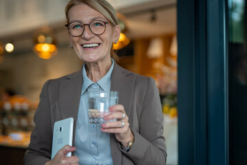 Mature businesswoman smiling, holding water and digital tablet