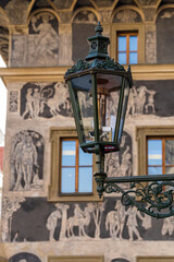 A vintage street lantern on an ornate bracket dominates the scene, set before a historic wall adorned with frescoes and arched windows, capturing urban heritag. Prague , Czech republic