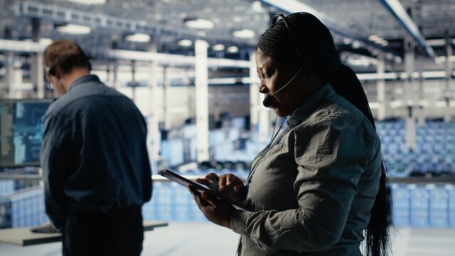 Server hub tech support expert guides enterprise clients through setting up secure company data backups. African american woman in data center helps users fix system errors on servers, camera B