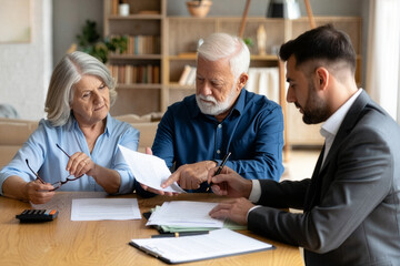 Mature couple consults with a male financial advisor, reviewing important papers at a wooden table