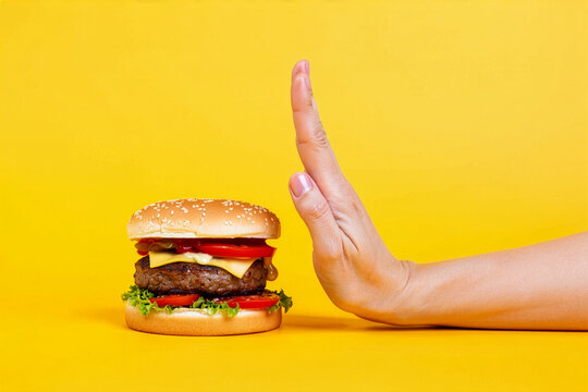 Hand gesturing stop to a hamburger on a bright yellow background