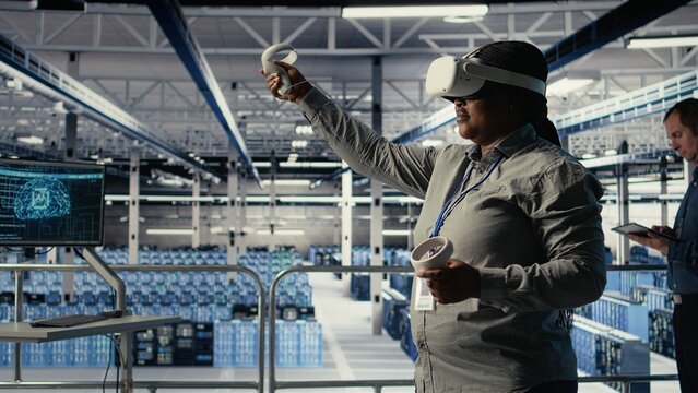 Software developer in server room wearing VR goggles optimizing deep learning systems handling tasks. African american woman in data center adjusts AI model parameters using virtual reality, camera A - Powered by Adobe