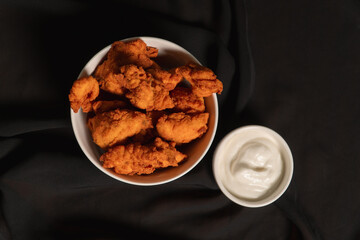 Top view of a bowl of fried chicken with white sauce on top of a black cloth.