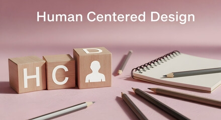 This stock photo illustrates the concept of human centered design with wooden blocks, notepad, and pencils on a pink surface, symbolizing innovation.