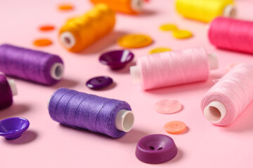 Colorful thread spools with buttons on pink background