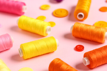 Colorful thread spools with buttons on pink background