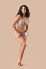 Naklejka premium Young African-American woman applying coconut oil to her leg on beige background