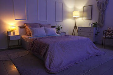 Fototapeta premium Interior of dark room with electric heating pad on bed and glowing lamps