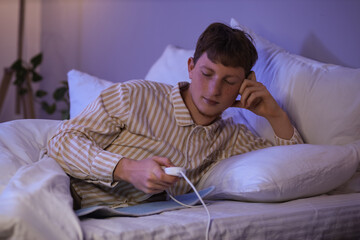 Fototapeta premium Young man turning on electric heating pad in bedroom at night