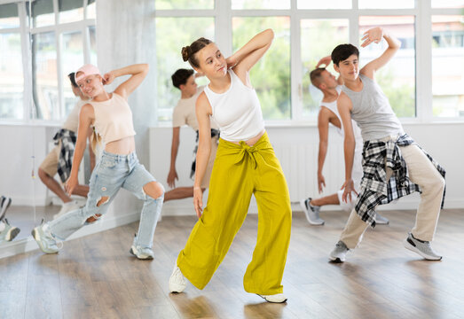 Positive teenage girl practicing hip hop backbend moves in training hall during group dancing classes - Powered by Adobe