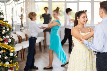 Smiling teenage girl enjoying slow dance with friend at school event during festive Christmas party with group of peers..