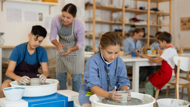 Pleased underage attendees of pottery circle working at throwing-wheel with female instructor