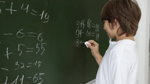Back to school. Boy doing math on chalkboard indoors