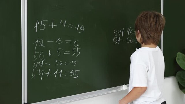 Back to school. Boy doing math on chalkboard indoors