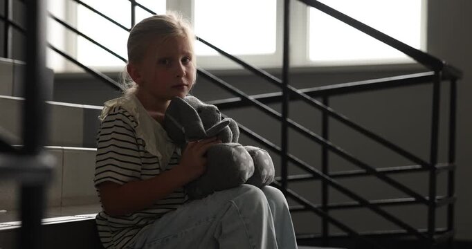 Sad little girl with toy bunny crying on stairs indoors