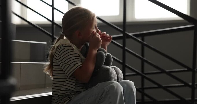Sad little girl with toy bunny crying on stairs indoors