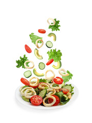 Squid rings and other ingredients falling onto plate with salad against white background