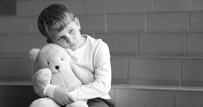 Upset little boy with toy bear on stairs indoors, black and white effect