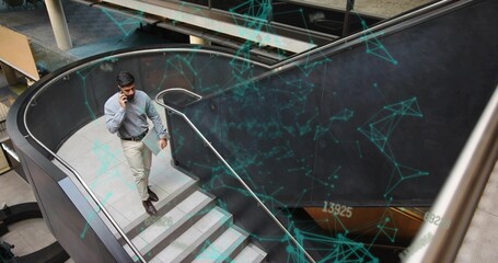 Ascending businessman using smartphone holding tablet on curved stairs in office atrium, copy space