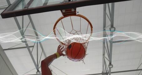 Shooting player wearing wristband sending basketball through hoop's net, under gym ceiling panels