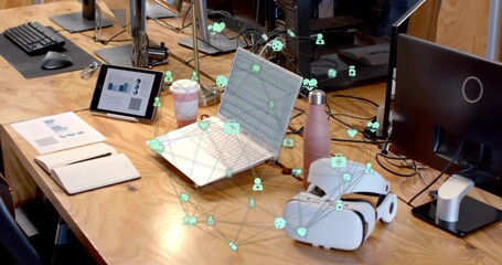 Displaying silver laptop with network icons overlay on office desk, with tablet and coffee cup © vectorfusionart