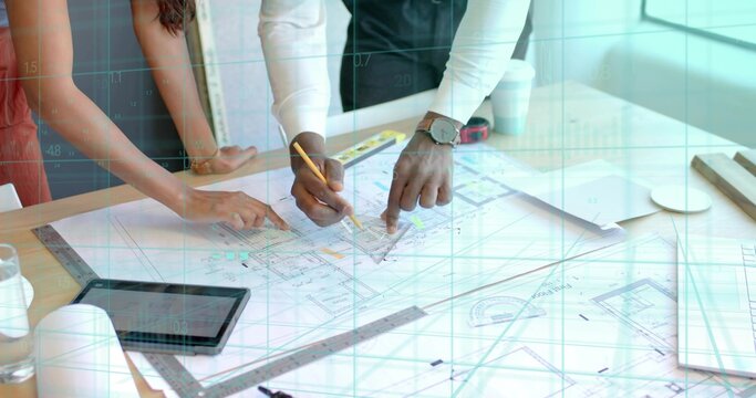 Pointing two architects leaning over wooden table in design studio, with blueprints pencil tablet