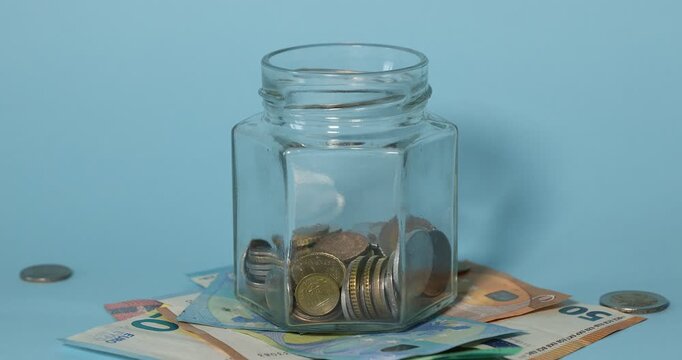 Coins falling into jar on light blue background, closeup. Money savings