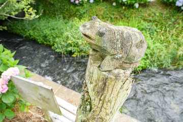 小川を見守る木彫りのカエルの像