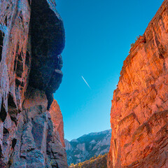 Centered composition with mountains & contrail from plane shows in white with blue sky.. This is morning with sun bouncing off cliff rocks in Cody, Wyoming, Buffalo Bill Park, near rock climbing area,