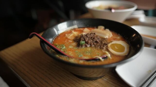 Close-up of spicy ramen served with spoon and napkins in cozy dining setting Hot ramen soup with egg and beef in black bowl on wooden restaurant table ramen 