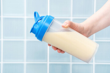 Female hand shakes shaker with protein cocktail on blue tile background.