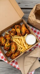 A cardboard box containing a variety of fried chicken wings, french fries, and a side of ranch dressing on a checkered tablecloth on a wooden table.