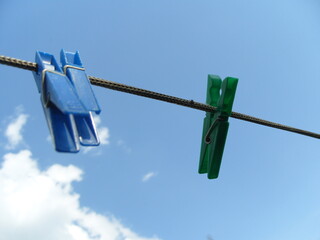 two blue clothespins on the left and one green clothespin on the right, all clipped onto a thin clothesline or wire. The diagonal line stretches across a clear blue sky with a few white clouds