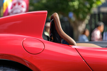 Sunlight creates alluring shadows on sports car's tan leather seat. White precision stitching runs up backrest's curved contour, flowing with smooth elegant line of the convertible's red body.