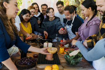 Group of Latin American Adult Students With Teacher Preparing recipe ingredients in Cookery Class in Mexico. Hispanic people multi generations learning together to cook in a terrace outdoors