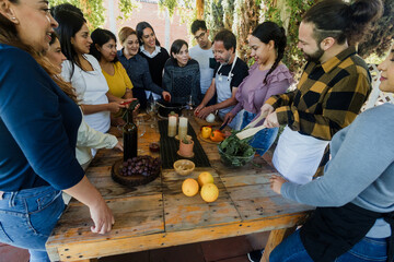 Group of Latin American Adult Students With Teacher Preparing recipe ingredients in Cookery Class in Mexico. Hispanic people multi generations learning together to cook in a terrace outdoors
