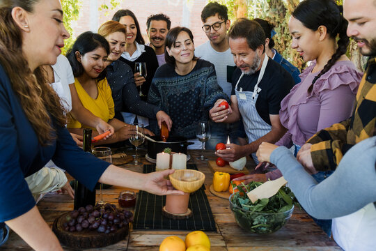 Group of Latin American Adult Students With Teacher Preparing recipe ingredients in Cookery Class in Mexico. Hispanic people multi generations learning together to cook in a terrace outdoors