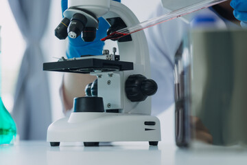 medical or scientific researcher researching and experimenting Multi-colored solution, vial and microscope In the laboratory or in the laboratory by wearing blue gloves and white clothing completely.