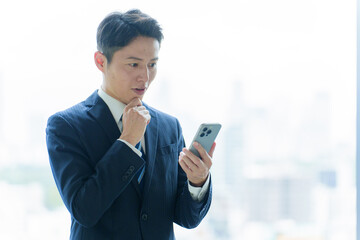 困った表情でスマートフォンを使うビジネスマン