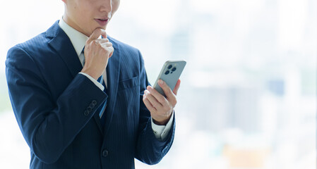 困った表情でスマートフォンを使うビジネスマン