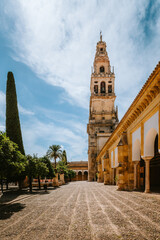 Obraz premium Mezquita Cathedral bell tower standing tall over the historic Patio de los Naranjos, showing ancient architecture and cobblestone path on a bright day in Cordoba, Andalucia
