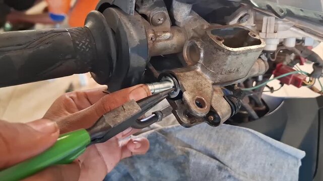 Close-up footage of a student mechanic repairing a motorcycle engine part using a hand tool during practical training in an automotive workshop.